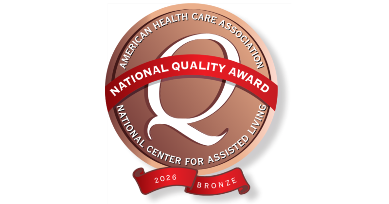 A circular award badge with a bronze-colored background, featuring the text "American Health Care Association" around the top and "National Center for Assisted Living" around the bottom. A red banner across the center reads "National Quality Award," and a smaller red ribbon at the bottom displays "2026" and "Bronze."