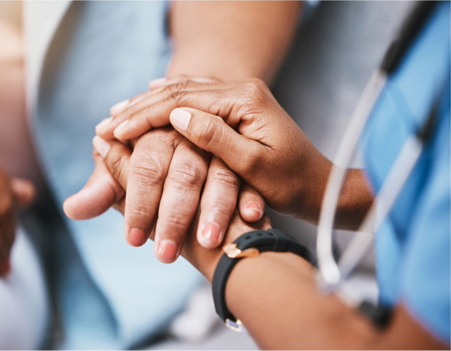 Close-up of a healthcare professional holding a patient's hand, with the professional wearing a stethoscope around their neck.
