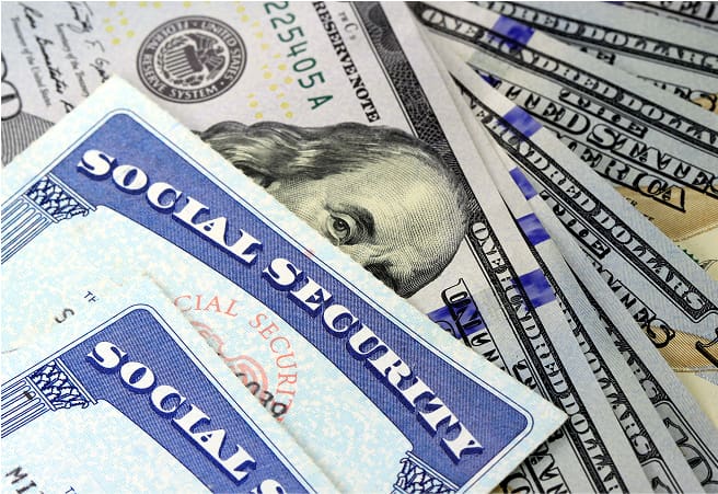 A close-up of Social Security cards overlapping U.S. dollar bills, including a fifty-dollar bill with a partial portrait of Ulysses S. Grant.